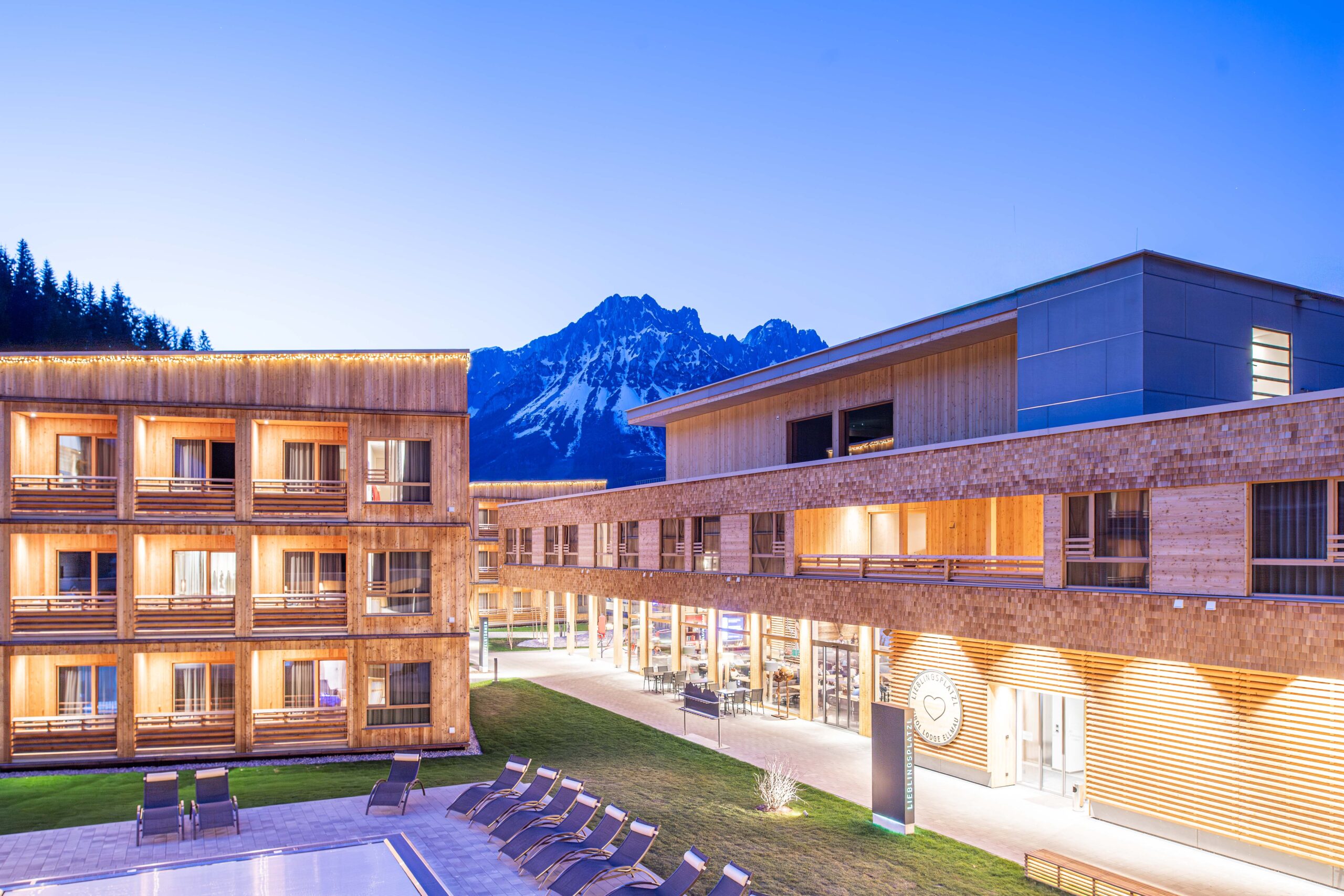 Referenz im Objektbau Hotelbau Holzbau Saurer | Tirol Lodge Ellmau Holzbau Nachtaufnahme Tourismus Abendstimmung Bergkulisse