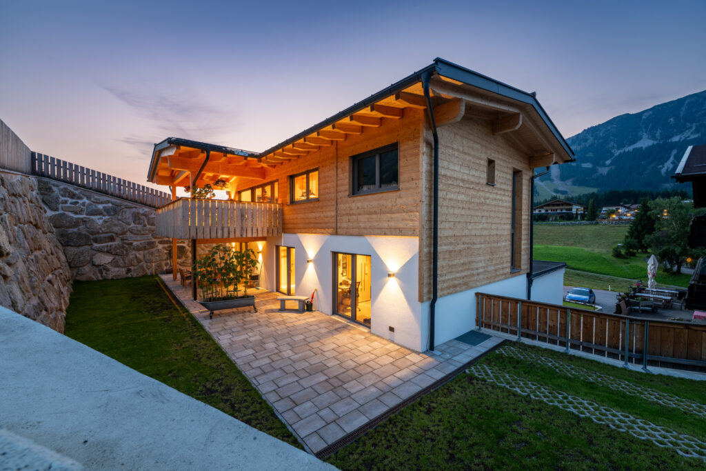 Referenz Holzbau Saurer Wohnbau Einfamilienhaus Außenaufnahme Perspektive Balkon Terrasse Garten in Hanglage Abendlicht Beleuchtung