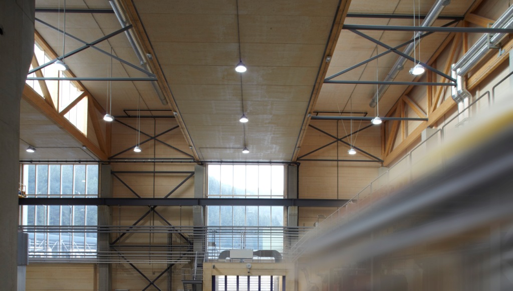 Innenansicht der Produktionshalle Oberflächentechnik der Plansee Group, realisiert von Holzbau Saurer – moderne Gewerbe- und Industriearchitektur aus Holz und Stahl mit heller Decke, sichtbarer Tragstruktur und funktional-ästhetischem Design.“