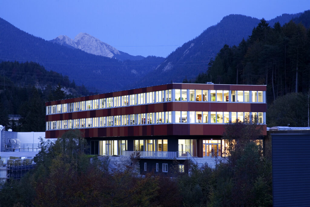 Holzbau Saurer Gewerbe- und Industriebau Ceratizit-Verwaltungsgebäudes ästhetische Holzarchitektur technische Funktionalität Nachhaltigkeit Arbeitsqualität Außenansicht bei Nacht – energieeffiziente Architektur mit klarer Gestaltung, innovativer Haustechnik und beleuchteter Fassade.