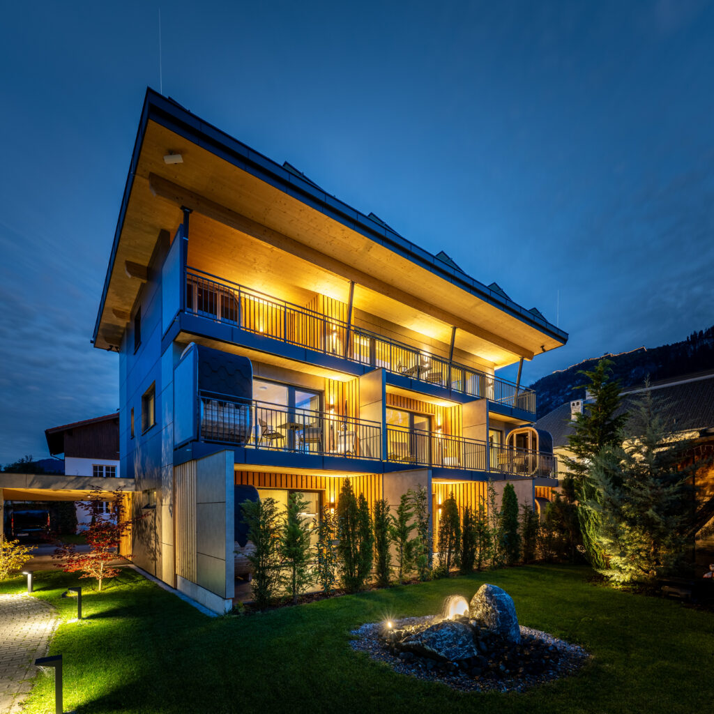 Holzbau Saurer Tinyhome Singer Aussenaufnahme Ansicht Balkone Gartenanlage Dämmerung Beleuchtung