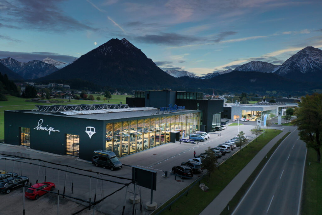 Referenz Holzbau Saurer Autohaus Schweiger Luftaufnahme moderner Objektbau nachhaltige Architektur Verglasung Dämmerungsaufnahme Beleuchtung eingebettet in Landschaft Gebirge